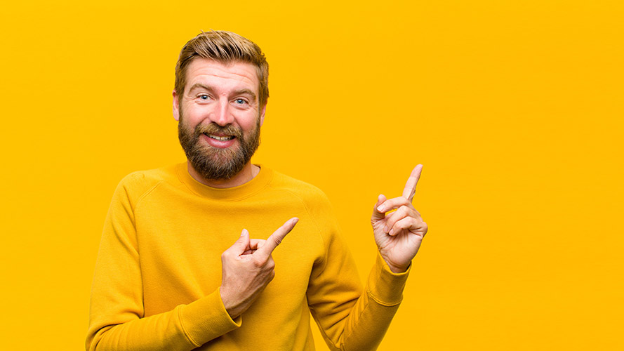 Lächelnder Mann mit orangefarbenem Pullover auf orangefarbenem Hintergrund, der mit dem Finger nach oben zeigt